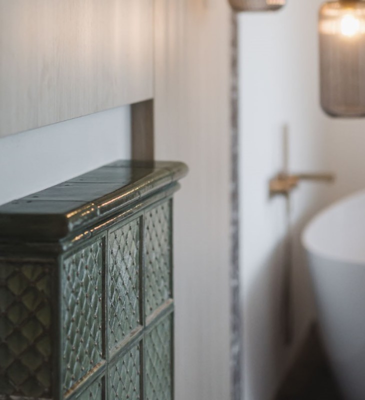 Nahaufnahme eines grünen, glasierten Kachelofens mit Muster in einem modernen Badezimmer mit freistehender Badewanne und hängender Lampe im Hintergrund