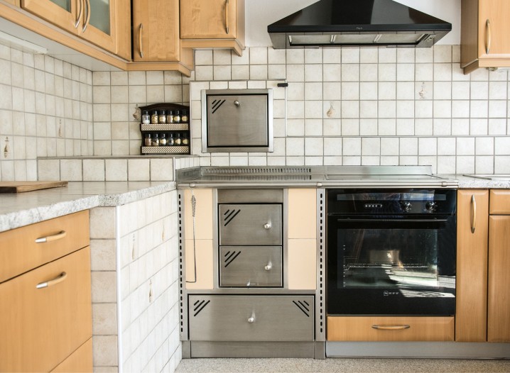 Küchenzeile mit Holzschränken, Fliesenspiegel, grauen Holzherd und schwarzen Backofen