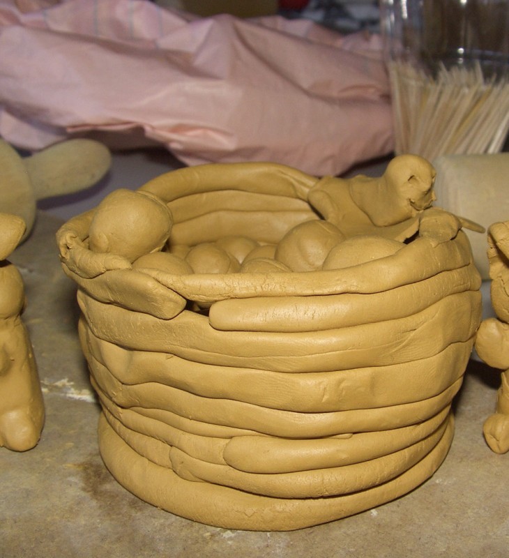 Tonkorb mit zwei Hasenfiguren und einer kleinen Kugel auf der Tischplatte