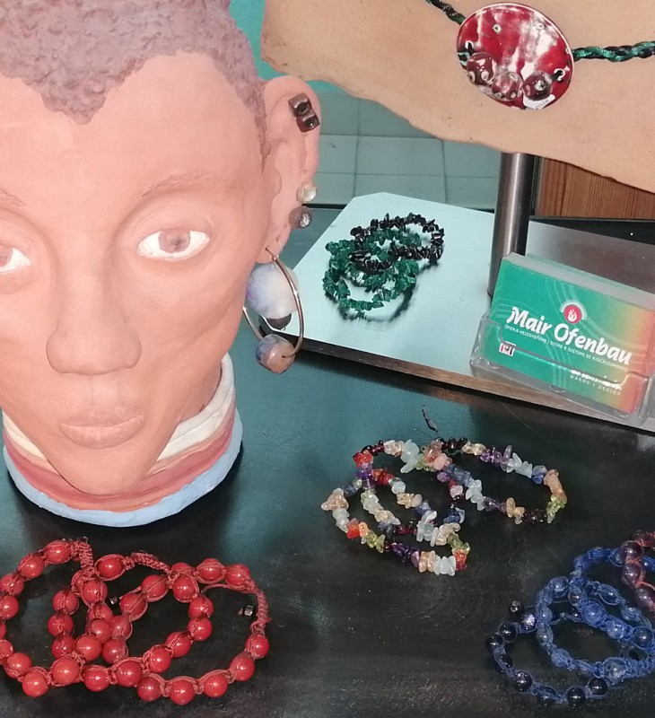 Mehrere bunte Armbänder aus Keramik Perlen und Steinen auf schwarzer Oberfläche und einem hellen Ständer