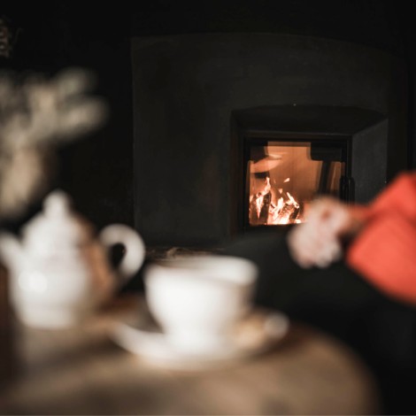 Unscharfe Nahaufnahme einer Tasse auf einem Tisch mit einem Kaminfeuer im Hintergrund und einer Person in rotem Oberteil