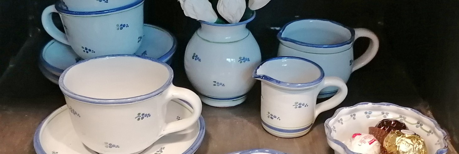 Porzellan-Kaffeegeschirr mit blauem Rand und kleinem Blumendekor, bestehend aus Tassen, Untertassen, Milchkännchen, Zuckerdose, Eierbecher und Vase mit künstlichen Blumen
