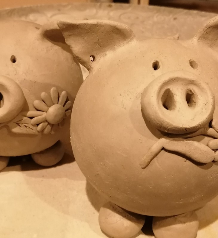 Zwei runde Tonfiguren in Form von Schweinen mit Blumen im Maul