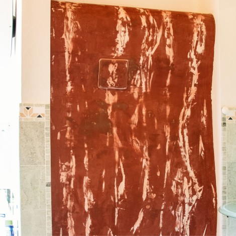 Großes, dunkelrote Ofenwand an einer weißen Badmauer mit einem kleinen, quadratischen Ausschnitt in der Mitte