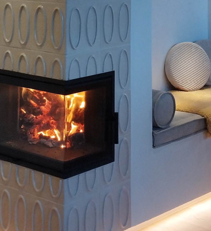 Eckkamin mit brennendem Feuer in einer Wand mit ovaler Musterung neben einer Sitznische mit Kissen und Decke