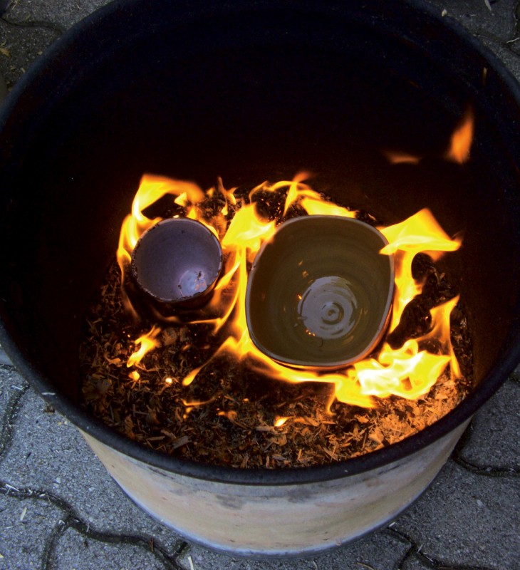 Feuer in einem Metallfass mit zwei Tontöpfen darin auf gepflastertem Boden