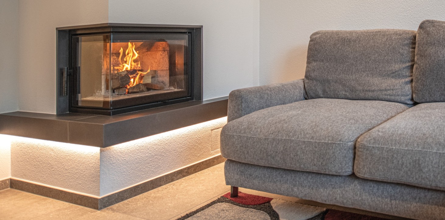 Eckkamin mit brennendem Feuer neben grauem Sofa auf Teppichboden