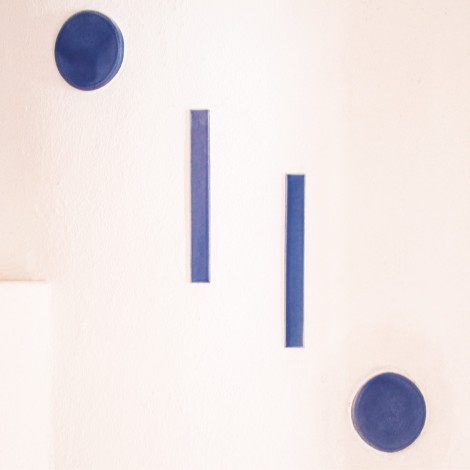 Handkeramik bestehend aus zwei blauen Kreisen und zwei blaue vertikale Rechtecke auf einer weißen Wand