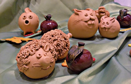 Tonfiguren in Tierform mit rundem Körper und detailreicher Oberfläche auf grünem Stoff drapiert