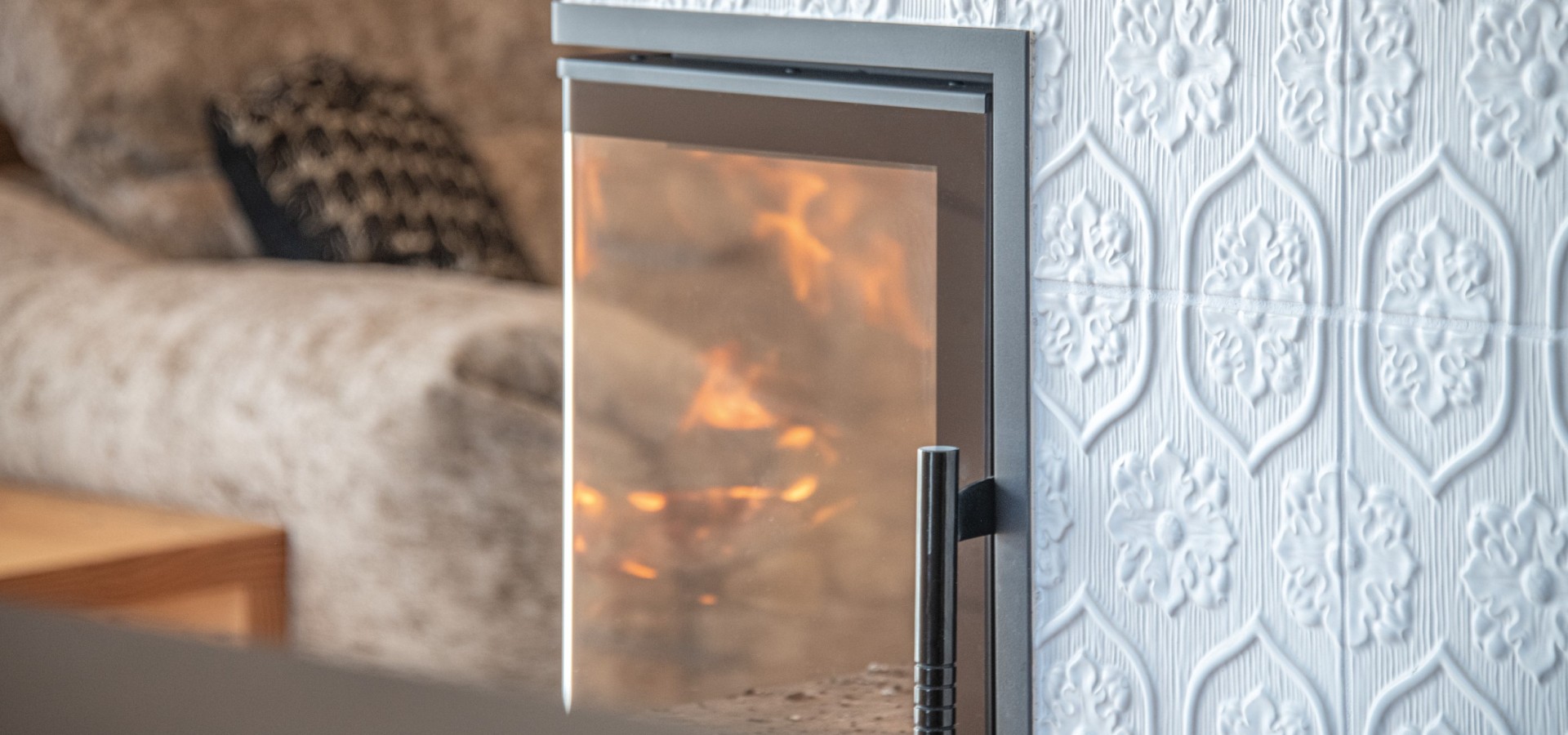 Nahaufnahme eines modernen Kamins mit sichtbarem Feuer und einer Wand mit dekorativem, strukturiertem Muster im Hintergrund