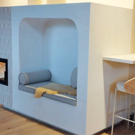 Moderner Ofen mit eingebauter Sitznische, rundem Kissen und Decke neben einem Bartisch mit zwei Holzstühlen