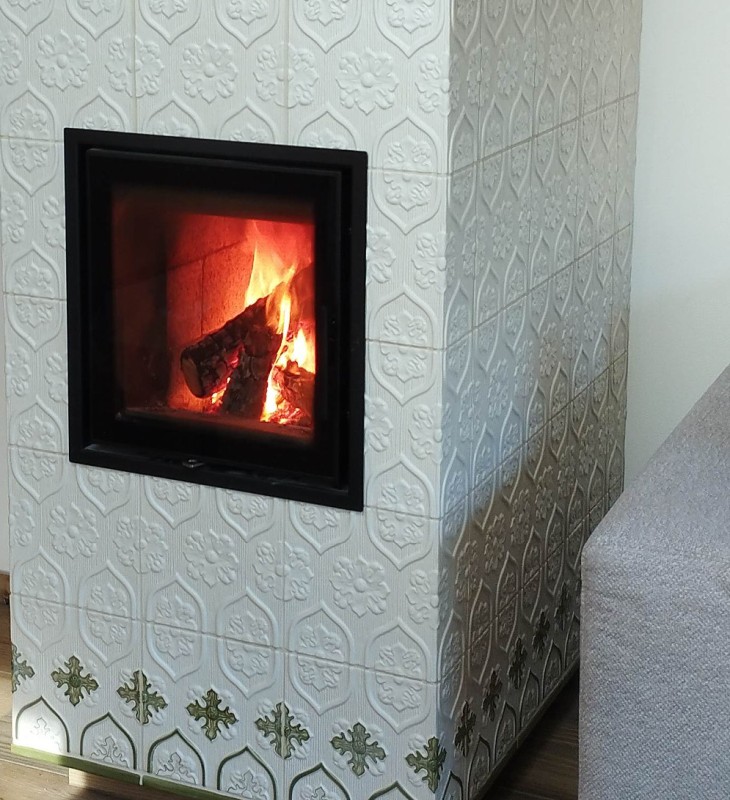 Kachelofen mit brennendem Holzfeuer neben grauem Sofa auf Holzboden