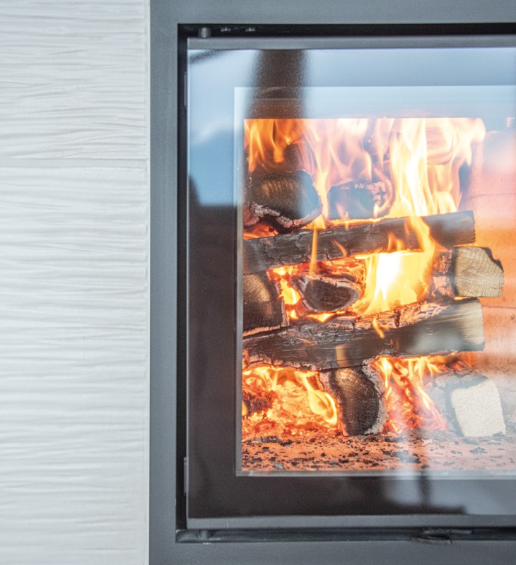 Brennender Kamin mit Holzscheiten hinter einer Glastür und weißer Wand mit Struktur