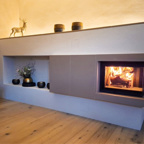 Moderner Kamin mit brennendem Feuer in einer weißen Wandnische, darüber Dekoration mit Hirschfigur und Vasen