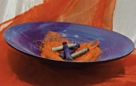 Blaues, flaches Gefäß mit orangenem Dekorationsmaterial und drei kleinen, zylindrischen Objekten darin